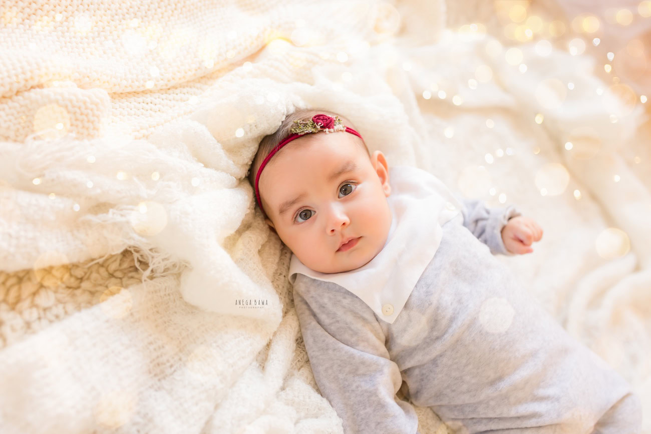 Baby girl photography, 6, 4, 3, or 5 months, white rug, golden lights, cute headband, beige backdrop. Location: Delhi, Gurgaon, Noida. Photographer: Anega Bawa.