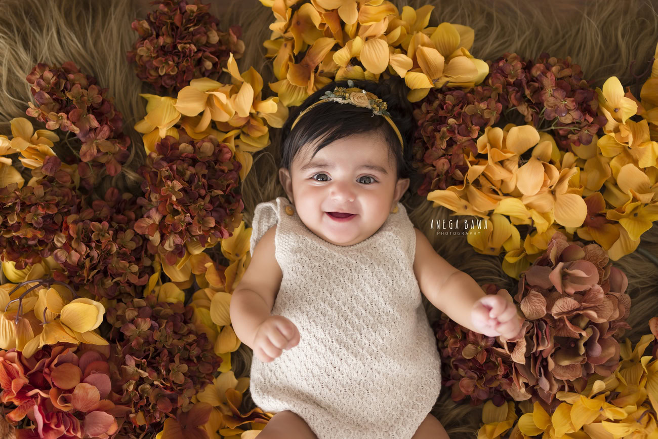 For a charming baby girl photoshoot at 3, 4, 5, or 6 months, adorn the backdrop with brown and yellow flowers and accessorize with a cute headband. Book your session with Anega Bawa in Delhi, Gurgaon, or Noida.