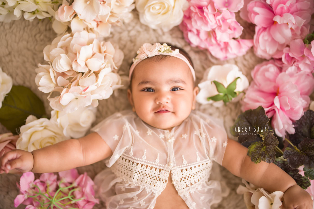 Indulge in the innocence of your little princess adorned in a cute net top and headband, complemented by multicolored flowers, against a soothing beige backdrop. Contact Anega Bawa for an exquisite photoshoot experience in Delhi, Gurgaon, or Noida.