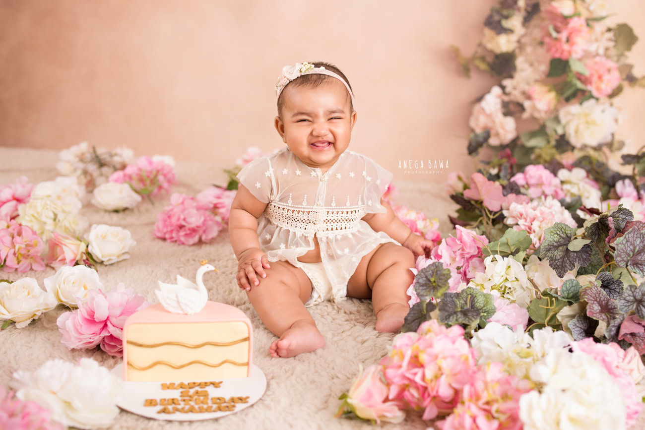 Capture the precious moments of your little angel in a delightful photoshoot featuring a cute net top, set against a charming peach backdrop and adorned with multicolored flowers, all atop a cozy beige rug. Contact Anega Bawa for a memorable cake smash session in Delhi, Gurgaon, or Noida.