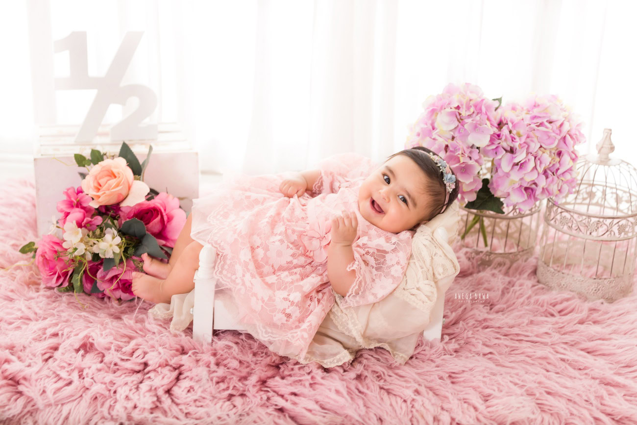 Capture the innocence and sweetness of your baby girl aged 3, 4, 5, or 6 months in a charming pink dress, adorned with a cute headband, resting on a soft pink rug. Contact Anega Bawa for your baby girl's photoshoot in Delhi, Gurgaon, or Noida.