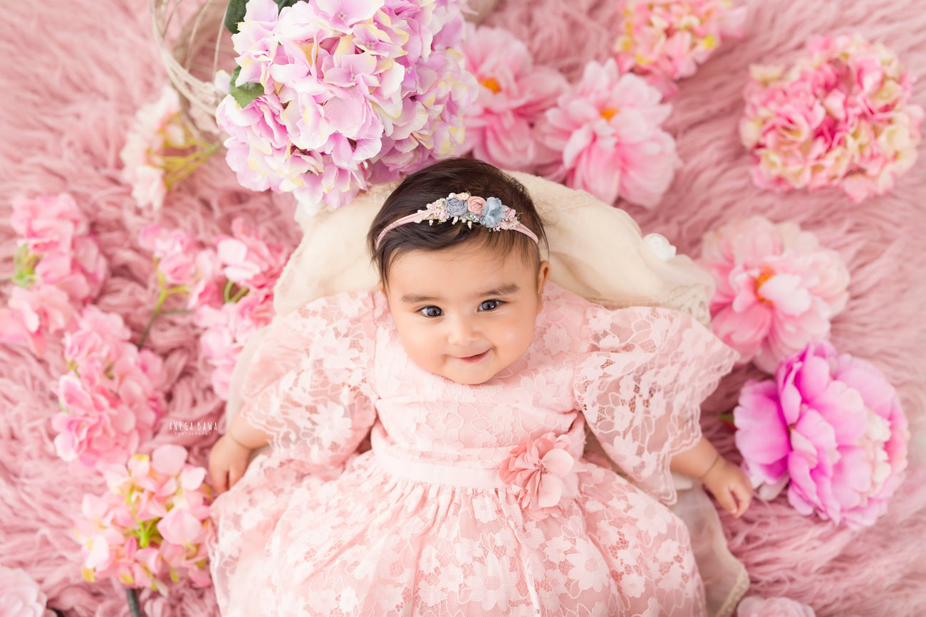 Capture the innocence and sweetness of your baby girl aged 3, 4, 5, or 6 months in a charming pink dress, adorned with a cute headband, resting on a soft pink rug. Contact Anega Bawa for your baby girl's photoshoot in Delhi, Gurgaon, or Noida.