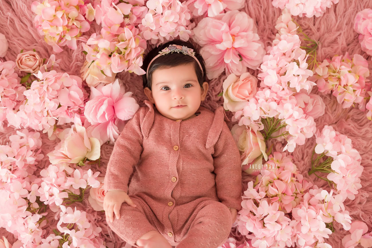 Baby girl photoshoot, 3, 4, 5, or 6 months, rusty pink rug, rusty pink baby suit, pink floral backdrop. Location: Delhi, Gurgaon, Noida. Photographer: Anega Bawa.