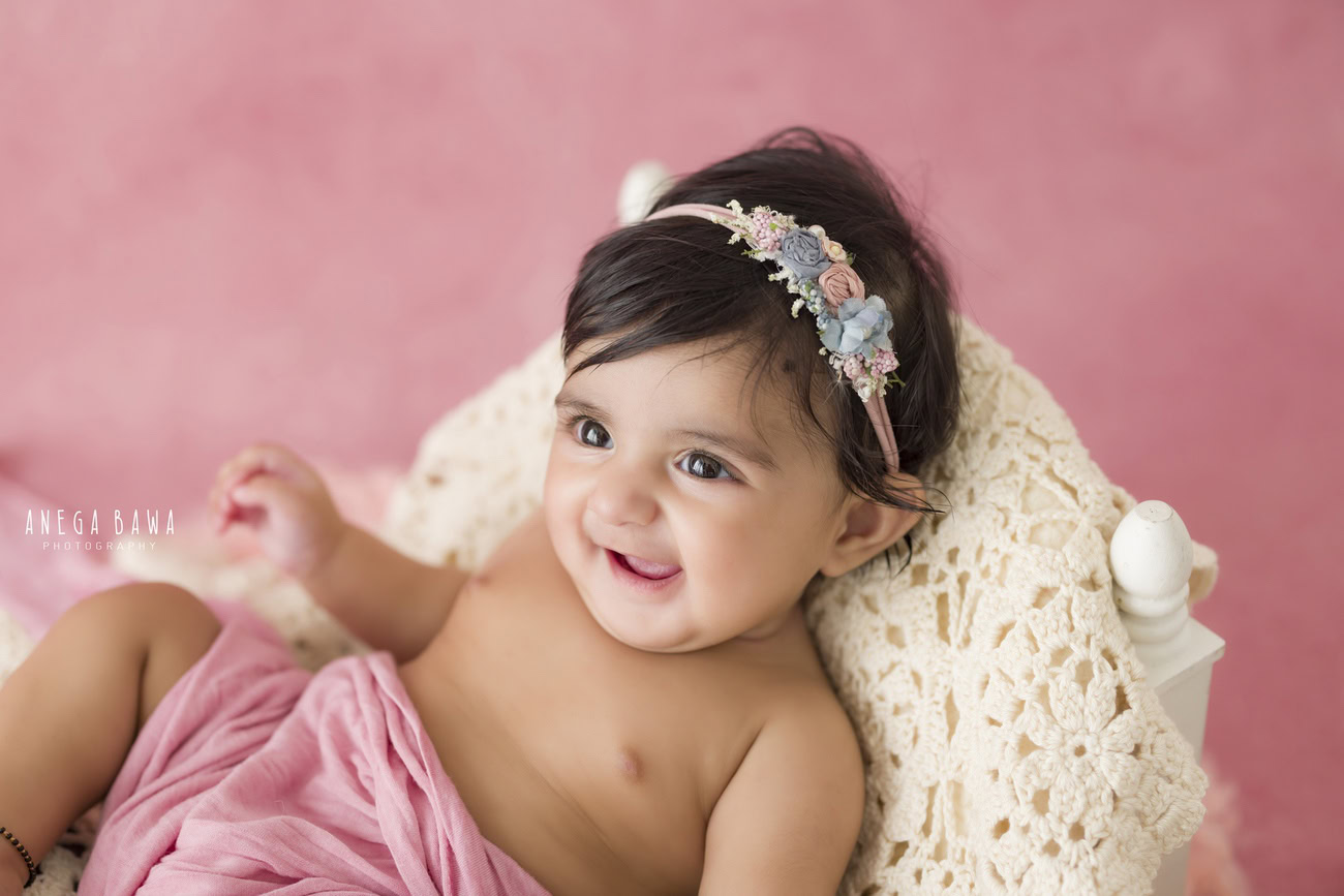 Baby girl photoshoot capturing the charm of a 3, 4, 5, or 6-month-old on a pink backdrop, wrapped in pink. Book your session with Anega Bawa in Delhi, Gurgaon, or Noida.
