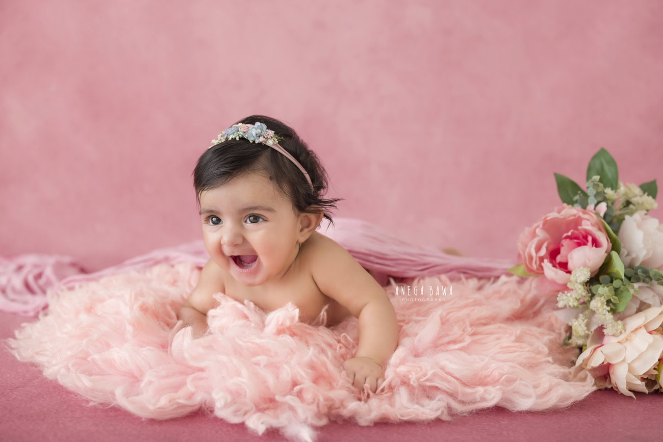 Capture your baby girl's precious moments at 3, 4, 5, or 6 months old with a charming pink rug, set against a pink backdrop adorned with flowers. Book your session with Anega Bawa in Delhi, Gurgaon, or Noida.