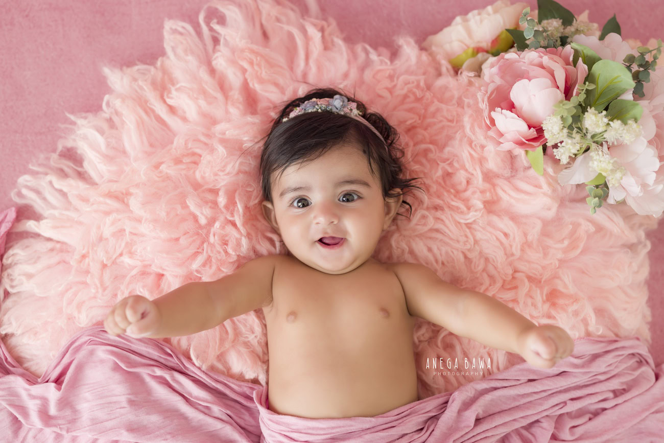 Capture your baby girl's charm at 3, 4, 5, or 6 months old with a pink rug and wrap, complemented by a cute headband. Book your photoshoot with Anega Bawa in Delhi, Gurgaon, or Noida.