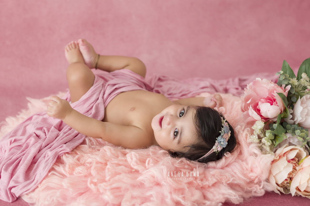 Celebrate your baby girl's milestones at 3, 4, 5, or 6 months with a delightful photoshoot featuring a pink rug, wrap, and backdrop. Contact Anega Bawa for this adorable session in Delhi, Gurgaon, or Noida.