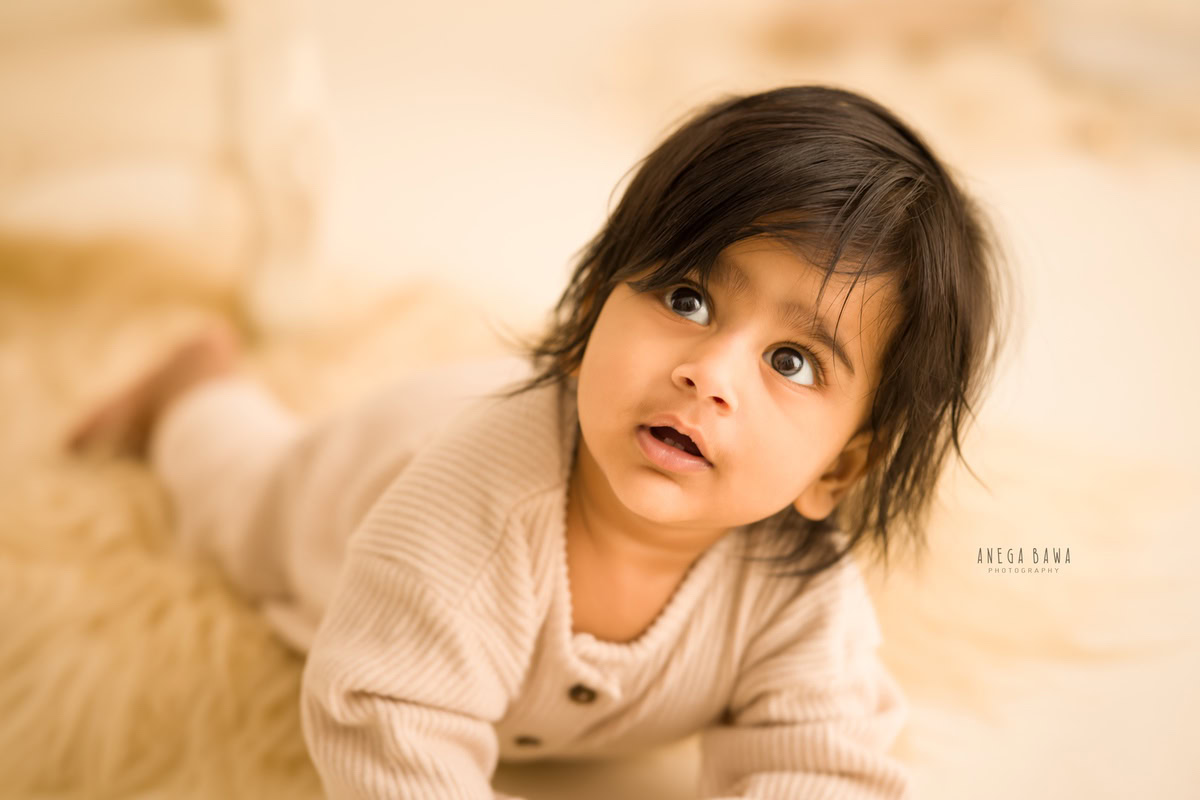 Indulge in the adorable innocence of a little boy, nestled on a cozy beige rug, against a calming beige backdrop. This heartwarming moment, perfect for a 8-9 months old, is beautifully captured in a sitter photoshoot in Delhi and Gurgaon.