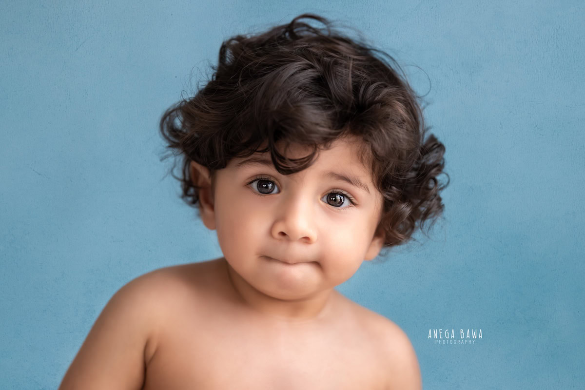 Captivating boy against a striking blue backdrop, immortalizing his joyful 8-9 months first birthday photoshoot in Delhi by Anega Bawa, Gurgaon, Noida