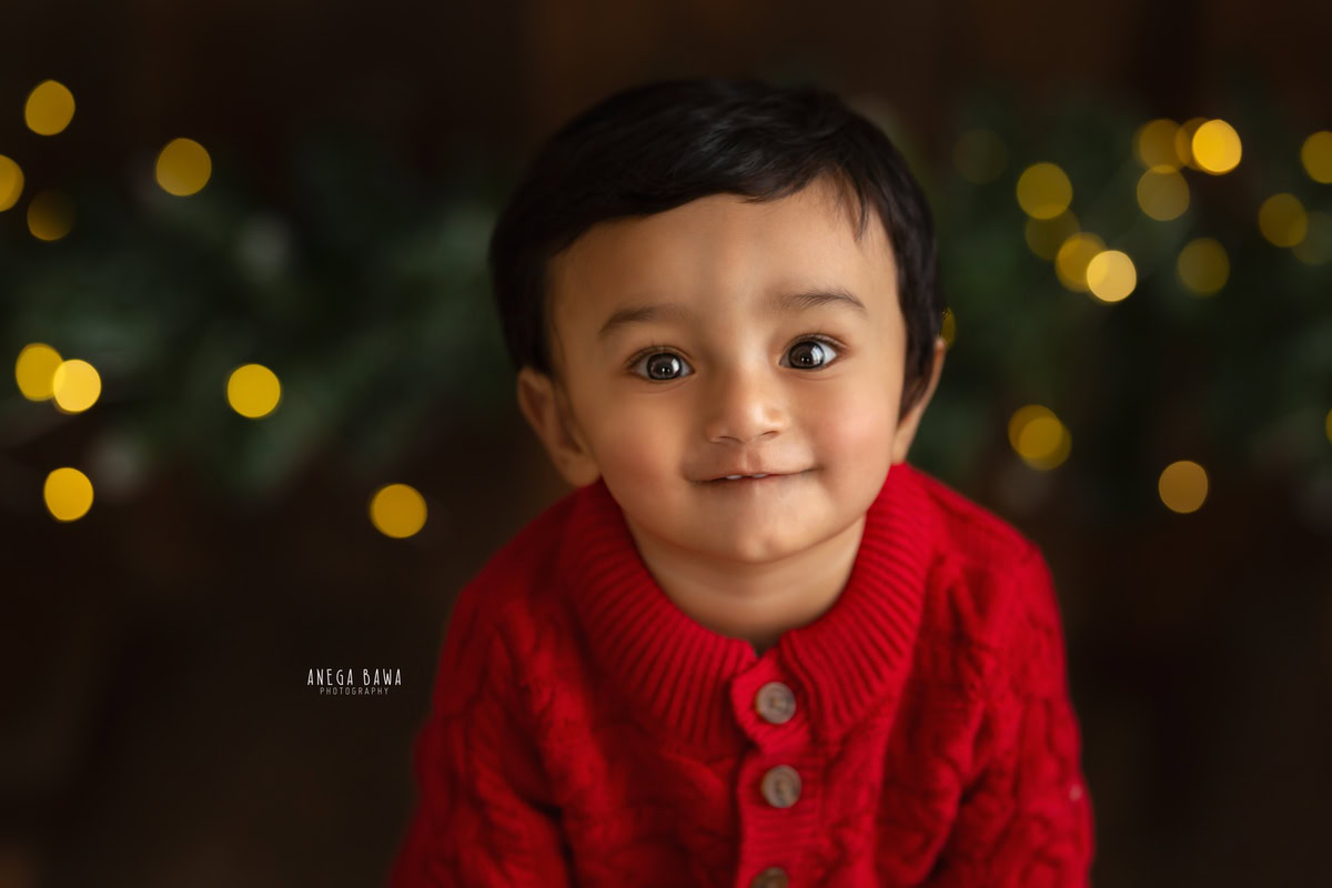 Immerse yourself in the enchanting ambiance as a young boy, aged 8-9 months, sits against a warm brown backdrop, adorned with golden lights casting a captivating bokeh effect. This picturesque setting captures the innocence and wonder of childhood, perfect for a sitter photoshoot in Delhi and Gurgaon.