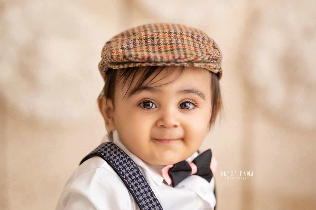 Capture the adorable charm of your 8-9-month-old boy in a sitter photoshoot by Anega Bawa Photography in Delhi and Gurgaon. Dressed in a stylish Burberry cap against a serene beige backdrop, every moment becomes a precious memory to cherish for years to come.