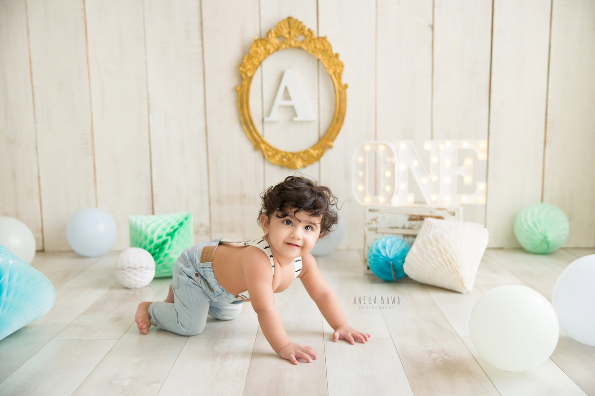 Celebrate the playful spirit of your 8-9-month-old boy with a captivating sitter photoshoot by Anega Bawa Photography in Delhi and Gurgaon. Against a chic beige backdrop adorned with vibrant balloons and whimsical pompoms, watch as he explores and crawls, creating cherished memories framed by an alphabet display on the wall.