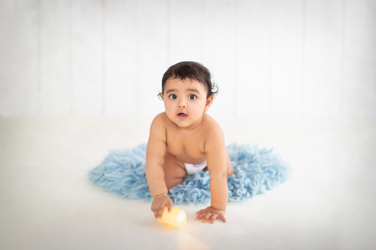 Create precious memories of your 8-9-month-old boy's journey with a sitter photoshoot by Anega Bawa Photography in Delhi and Gurgaon. Against a pristine white backdrop, capture him as he explores on a soft blue rug, every crawl a step towards adventure and discovery.