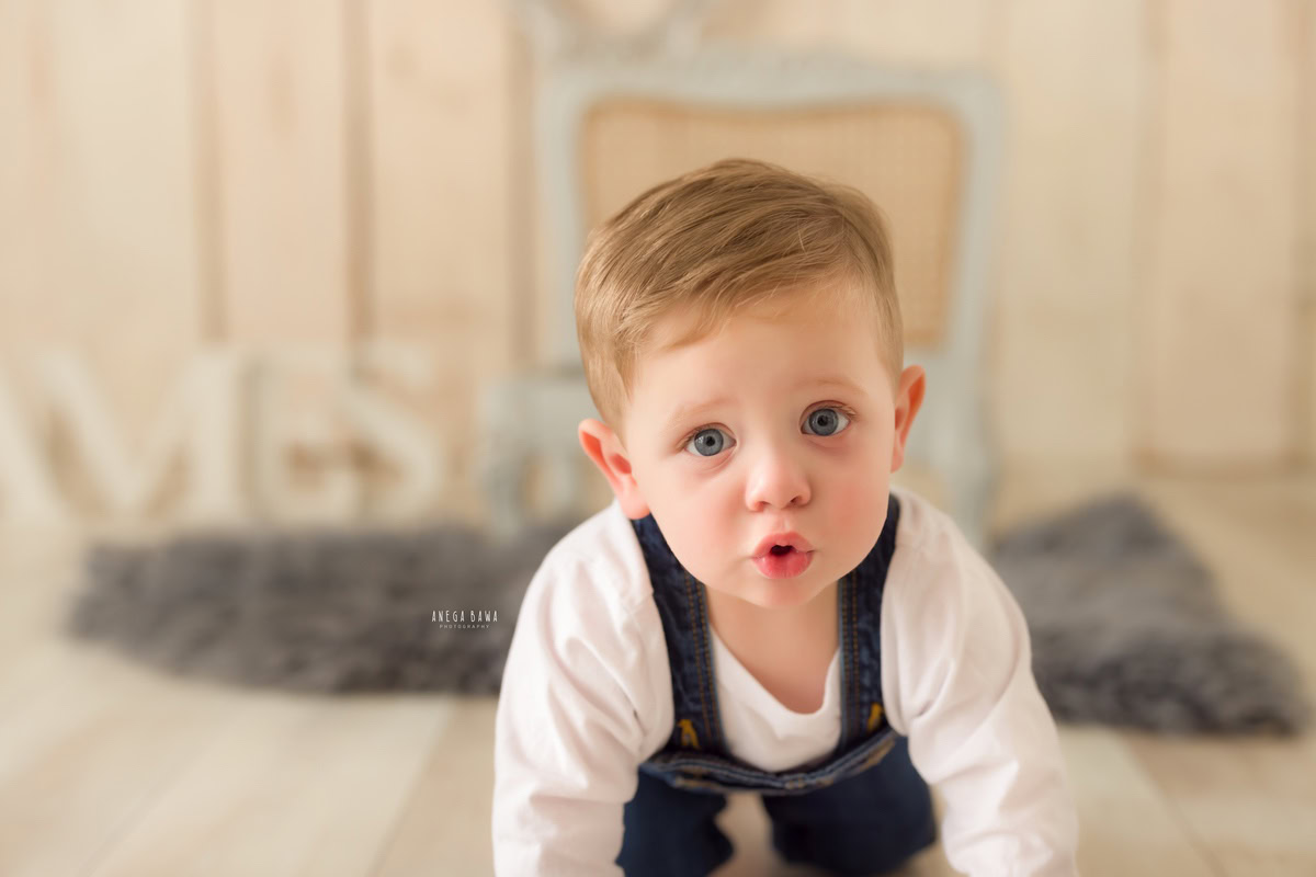 In this endearing shot from a baby pre-birthday photoshoot by Anega Bawa in Delhi, an adorable 8-month-old boy strikes a playful pout while joyfully crawling on a soft grey rug. The soothing beige backdrop provides a serene setting, highlighting the innocence and charm of this precious moment.
