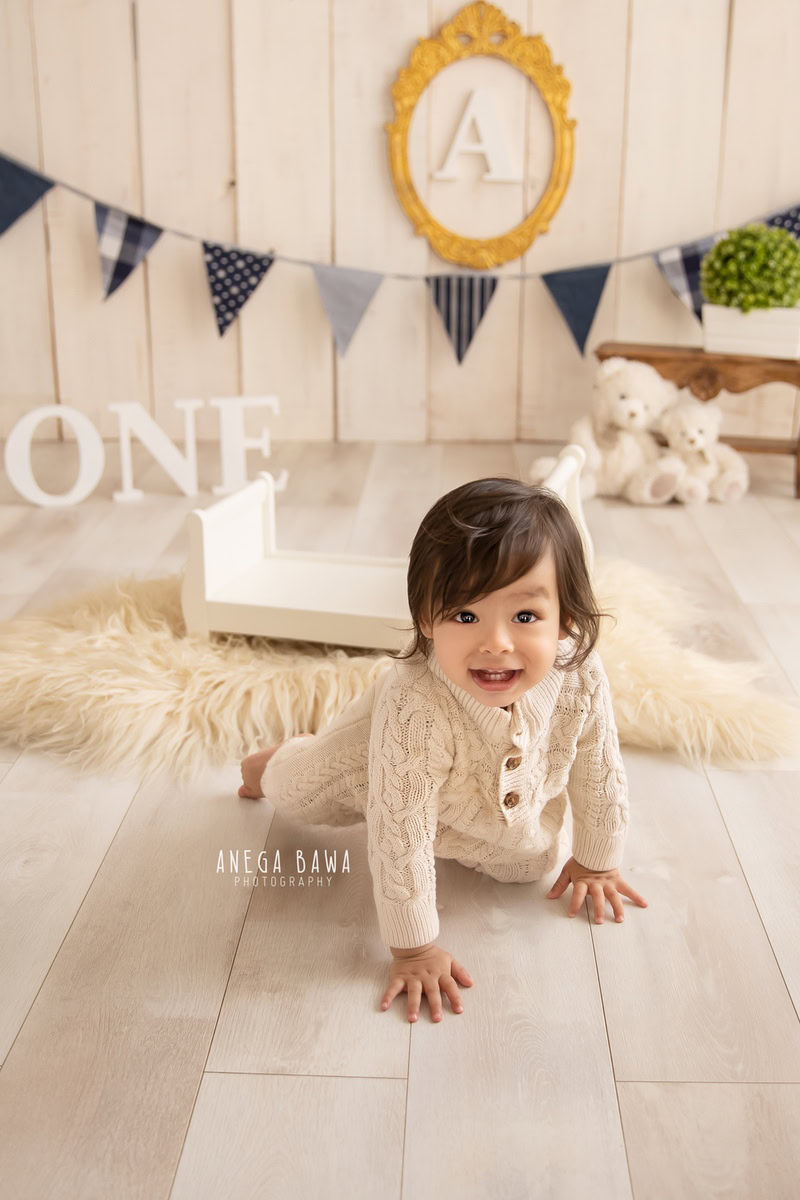 Capture the curiosity of an 8-month-old boy as he crawls on a soft beige rug, surrounded by teddy bears and an alphabet frame adorning the wall against a soothing beige backdrop. This charming scene is perfect for a sitter photoshoot in Delhi and Gurgaon, preserving these precious moments of exploration and discovery.