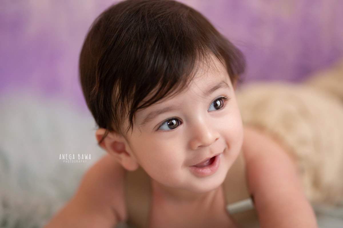 Capture the innocence of your 9-month-old boy with a sitter photoshoot by Anega Bawa Photography in Delhi and Gurgaon. Let him shine in adorable lying poses on a cozy beige rug against a lavender backdrop, creating timeless memories of his early months.