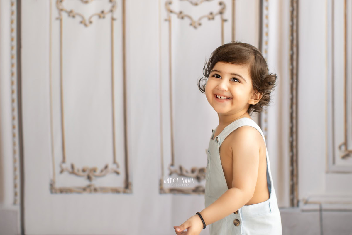 Captured during a sitter photo shoot in Delhi, Gurgaon by the talented Anega Bawa, this adorable 9-month-old boy shines in denim dungarees against a striking white backdrop.