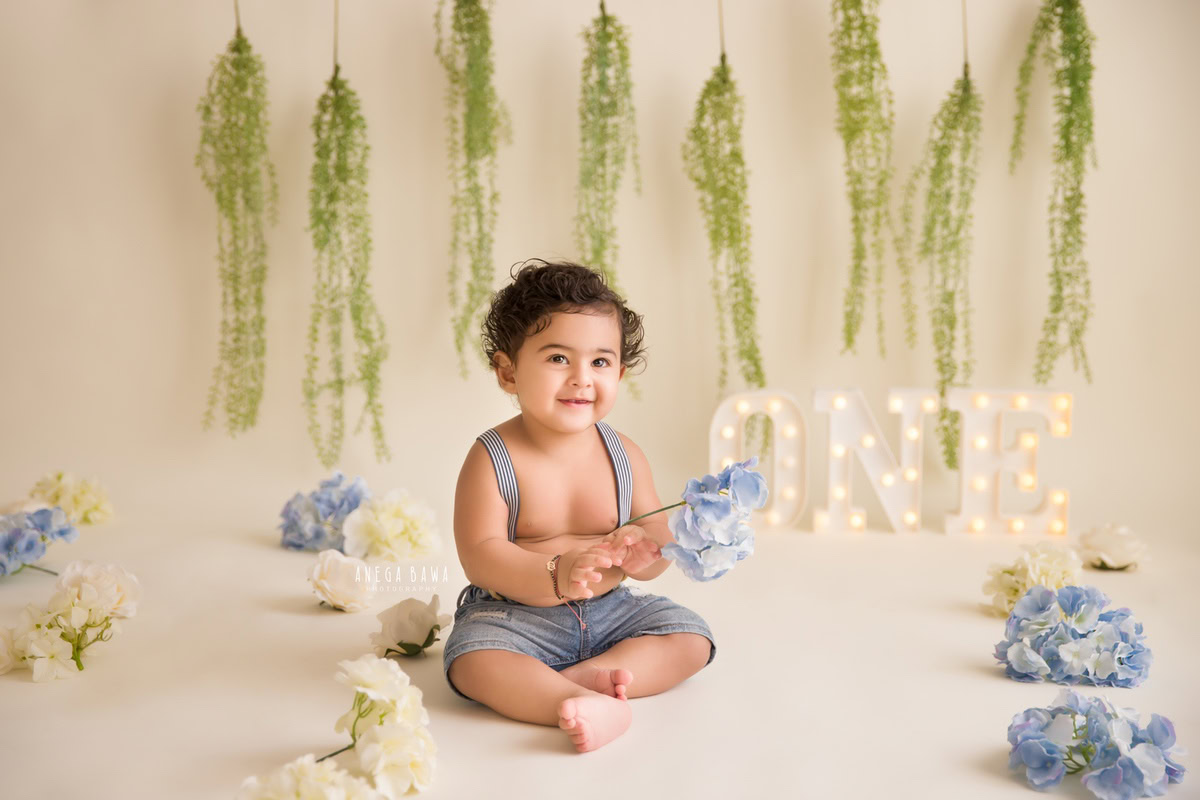 In an enchanting portrait by sitter photographer Anega Bawa in Delhi, a cherubic 9-month-old boy holds a delicate flower against a serene beige backdrop, with leafy fringes adorning the wall and blue flowers scattered on the floor.