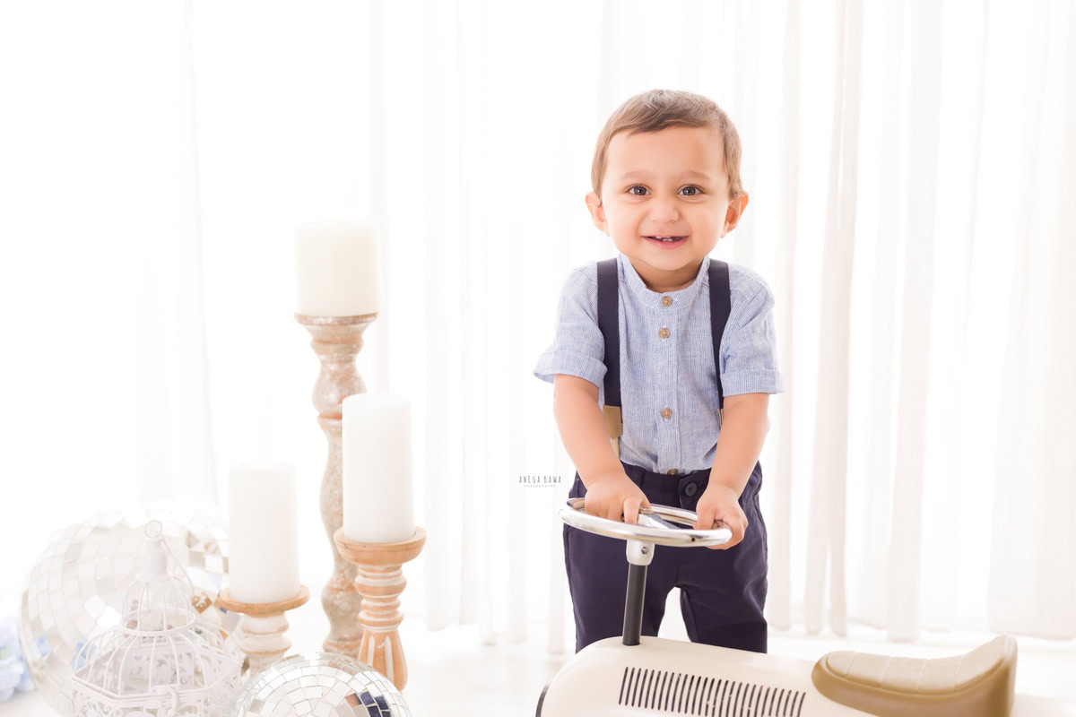 Captivating boy holding a toy scooter beside a candle stand against a pristine white backdrop, commemorating his adorable 9 months first birthday photoshoot in Delhi by Anega Bawa, Gurgaon, Noida