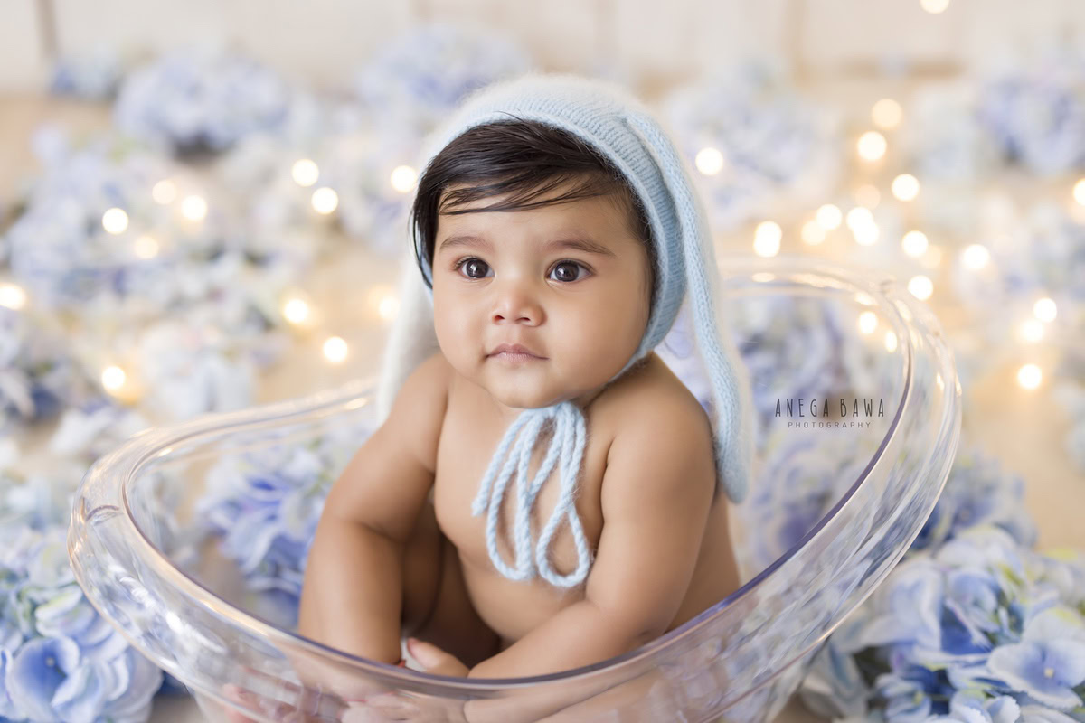 Captivating boy in a crystal tub adorned with blue flowers and a charming blue cap, illuminated by golden lights, celebrating his 10 months first birthday photoshoot in Delhi by Anega Bawa, Gurgaon, Noida