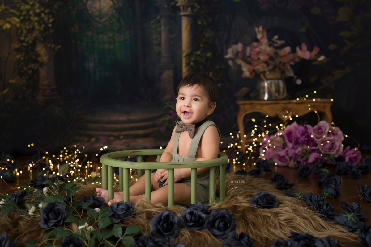 During this enchanting baby pre-birthday photoshoot in Delhi, expertly captured by Anega Bawa, a delightful 11-month-old boy reclines in a charming green cot. Adorned with whimsical flowers and surrounded by twinkling fairy lights, he exudes joy and innocence against a warm brown backdrop, creating a magical scene that will be treasured for years to come.