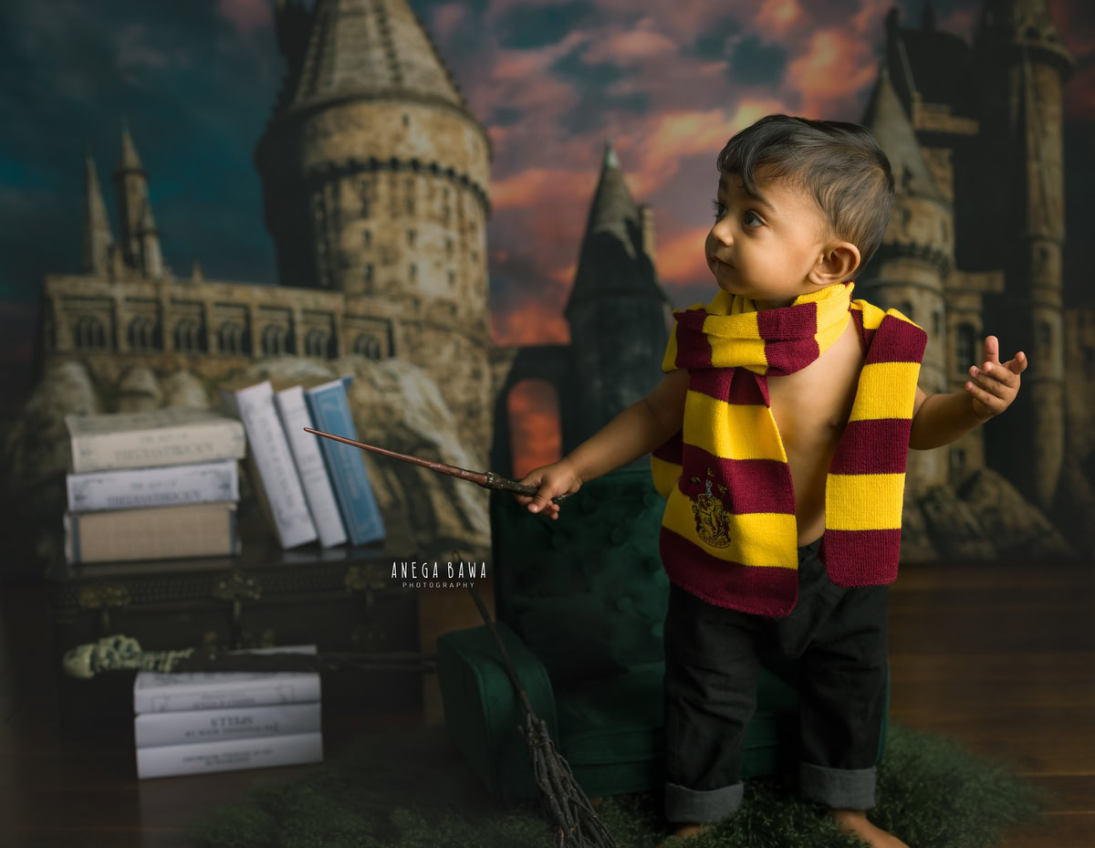 Step into the magical realm of Anega Bawa Photography's sitter photoshoots in Delhi and Gurgaon. Picture your 11-month-old boy adorned in a Harry Potter-inspired outfit, clutching a wooden stick and surrounded by books, set against an enchanting orange cloudy backdrop. These whimsical moments capture the essence of childhood wonder and imagination.