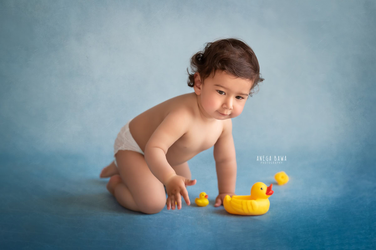 In this delightful moment captured during a sitter photo shoot in Delhi, Gurgaon by Anega Bawa, an 11-month-old boy looks adorable in his Pampers. Against a serene blue backdrop, he's accompanied by a cute Tweety toy, adding a playful touch to the scene.