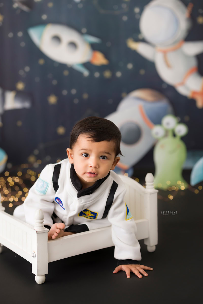 Adorable boy nestled in a white cot against a mesmerizing space backdrop, commemorating his 11 months first birthday photoshoot in Delhi by Anega Bawa, Gurgaon, Noida