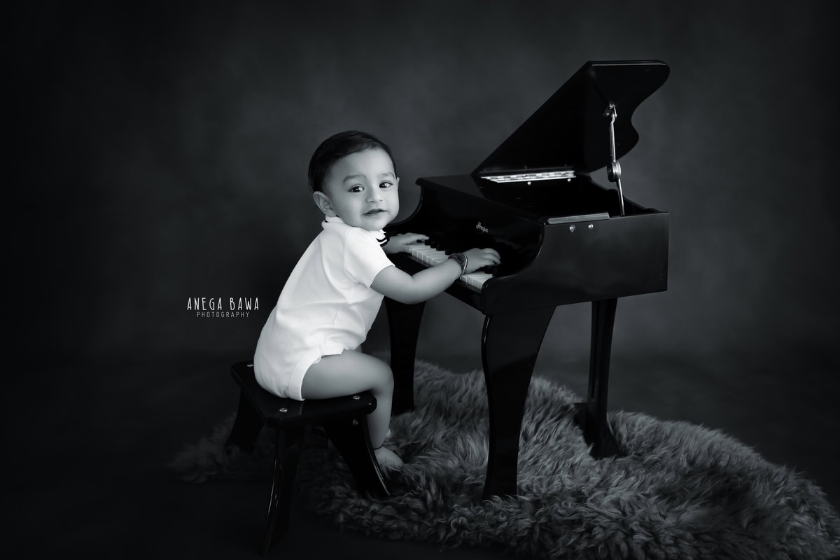 In Gurgaon, Anega Bawa, a skilled sitter photographer, immortalizes the joyful moments of a 13-month-old boy as he discovers the magic of music, playing the piano with enthusiasm. The striking contrast of the black and white backdrop perfectly complements the warmth of the brown rug, adding depth to the captivating scene.