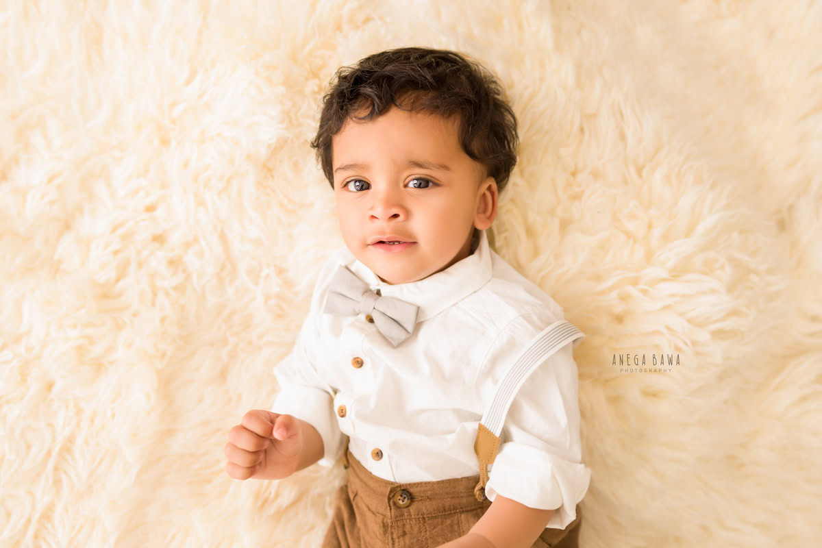 Captivating boy posing on a cozy beige rug against a serene beige backdrop, commemorating his 13 months first birthday photoshoot in Delhi by Anega Bawa, Gurgaon, Noida