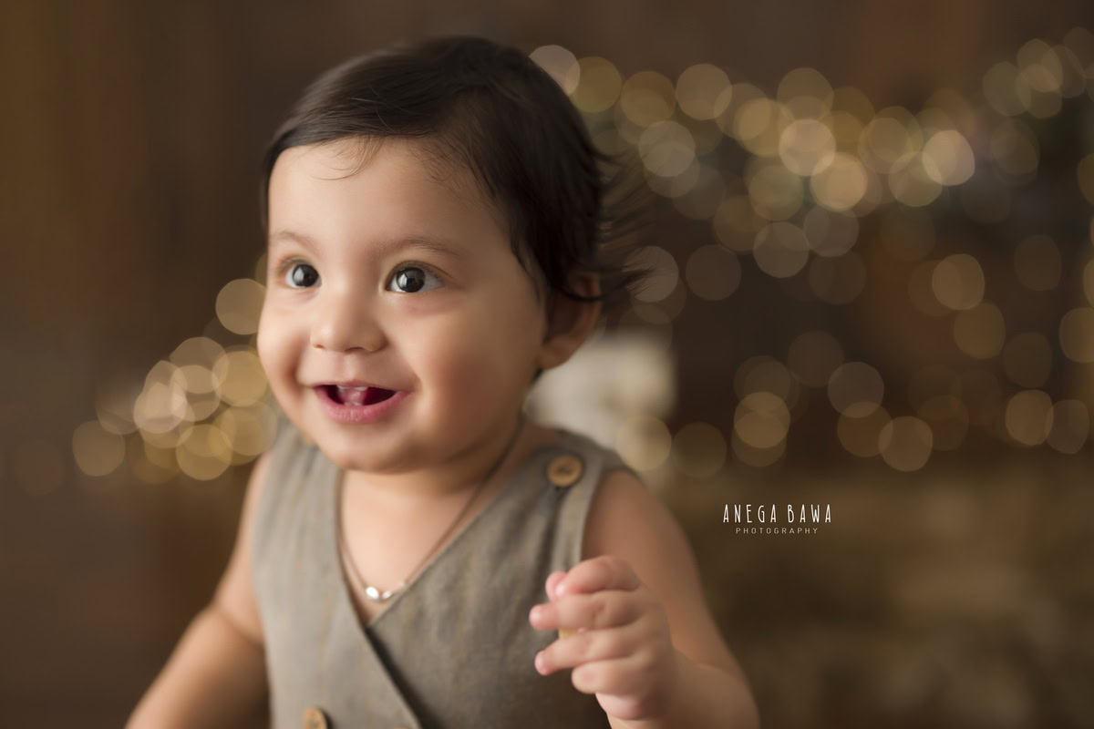 Capture the charm of your 13-month-old boy with Anega Bawa Photography's sitter photography in Delhi and Gurgaon. Picture him seated against a warm brown backdrop, illuminated by twinkling fairy lights. These magical moments preserve his innocence and wonder for years to come.