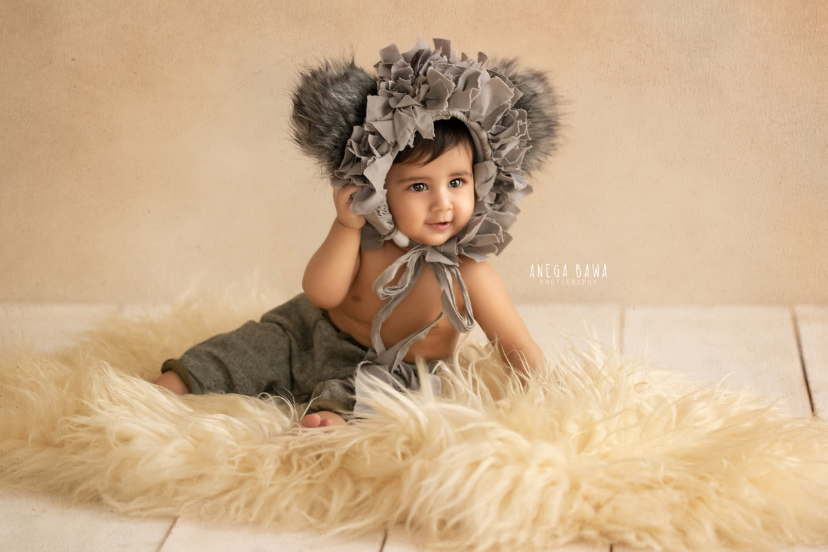 In the delightful sitter photoshoot captured by Anega Bawa in Delhi, Gurgaon, this 14-month-old boy showcases his unique style as he sits on a beige rug. With a charming grey cap adding to his adorable look, against a soothing beige backdrop, every moment is a treasure to behold.