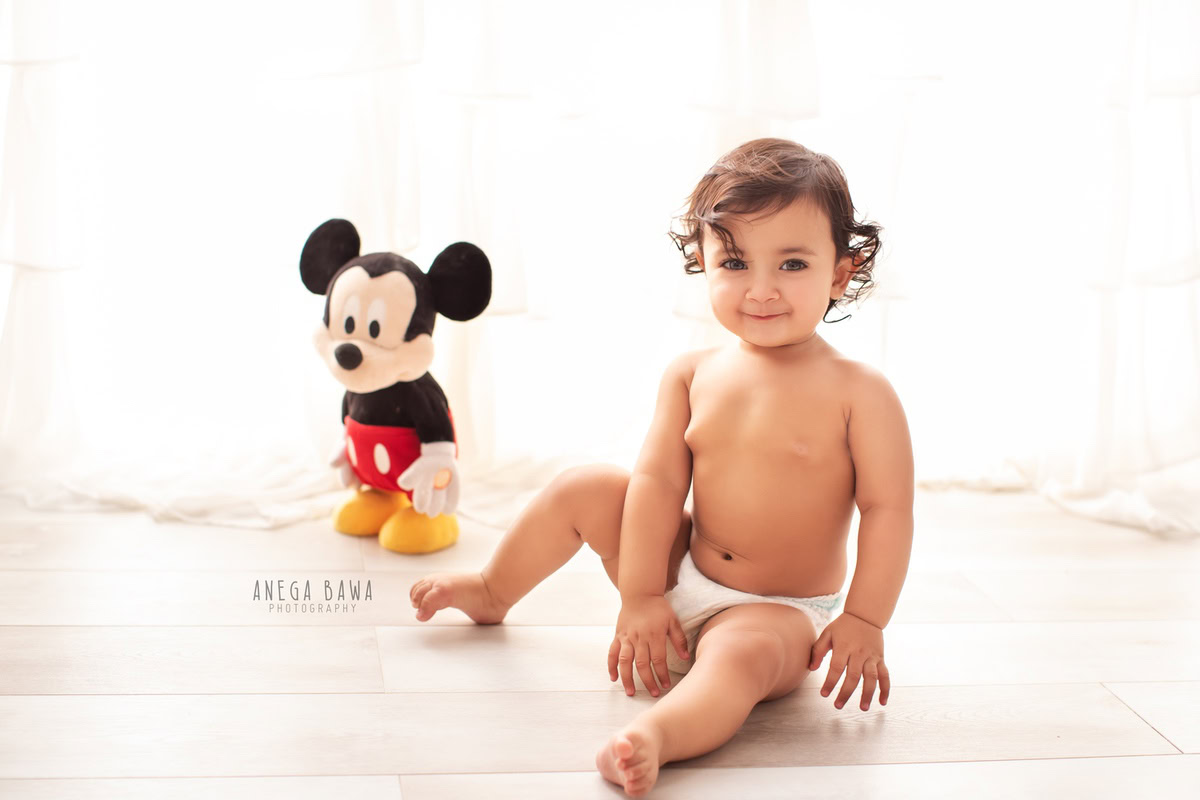 Capture the joy of your 15-month-old boy's sitter milestone with Anega Bawa Photography in Delhi and Gurgaon. Seated on the floor surrounded by Mickey Mouse soft toys, against a pristine white backdrop, these photos will be cherished memories of this special moment in his early years.