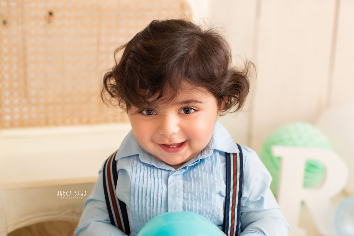 Create timeless memories with your 15-month-old boy through a sitter photoshoot by Anega Bawa Photography in Delhi and Gurgaon. Set against a soft beige backdrop adorned with playful pompoms, these photos capture the charm and innocence of childhood.