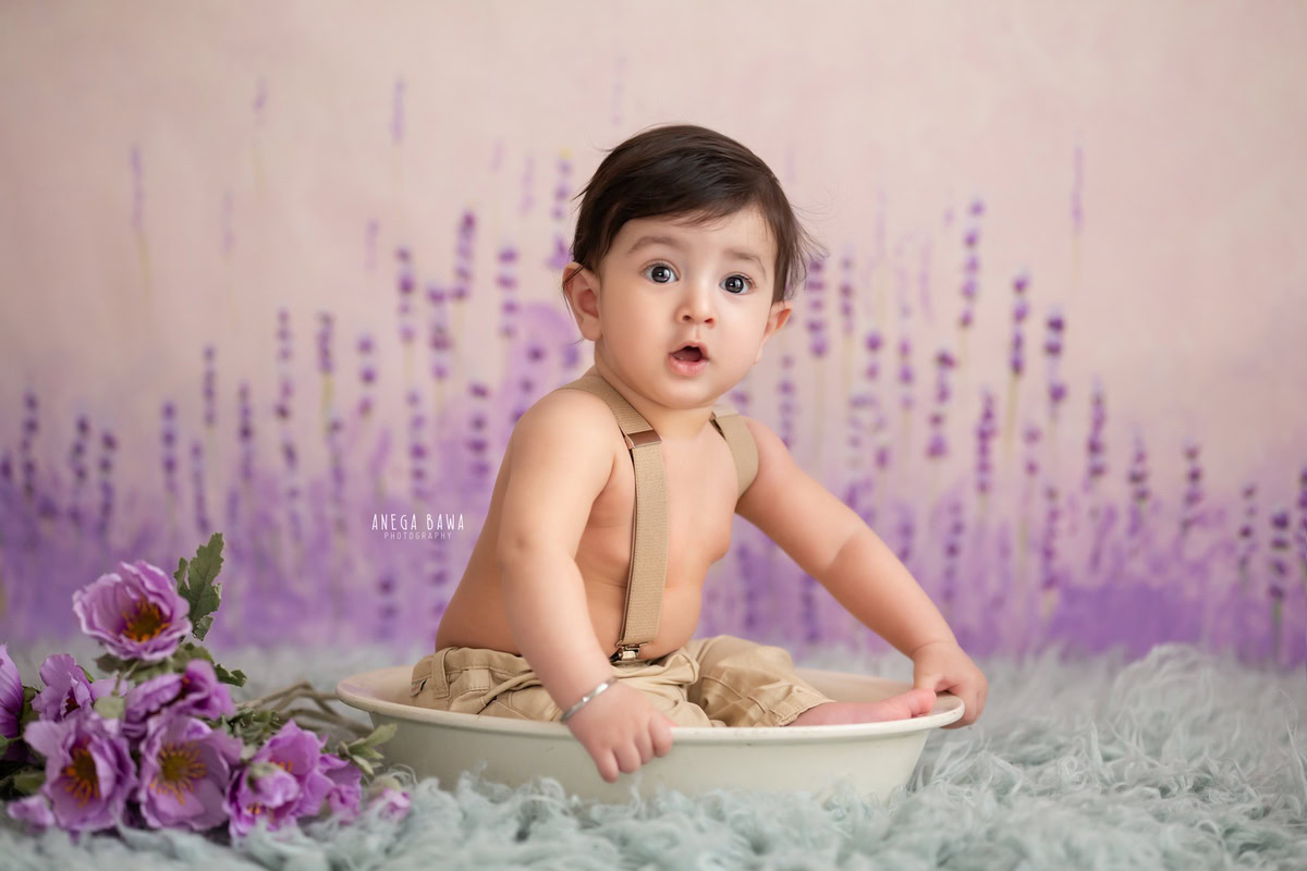 Capture the precious moments of your 10-month to 1-year-old boy with a sitter photoshoot by Anega Bawa Photography in Delhi and Gurgaon. Let him sit comfortably in a white tub, against a soothing lavender backdrop, adorned with a bunch of flowers, creating a serene and charming atmosphere for the photoshoot.