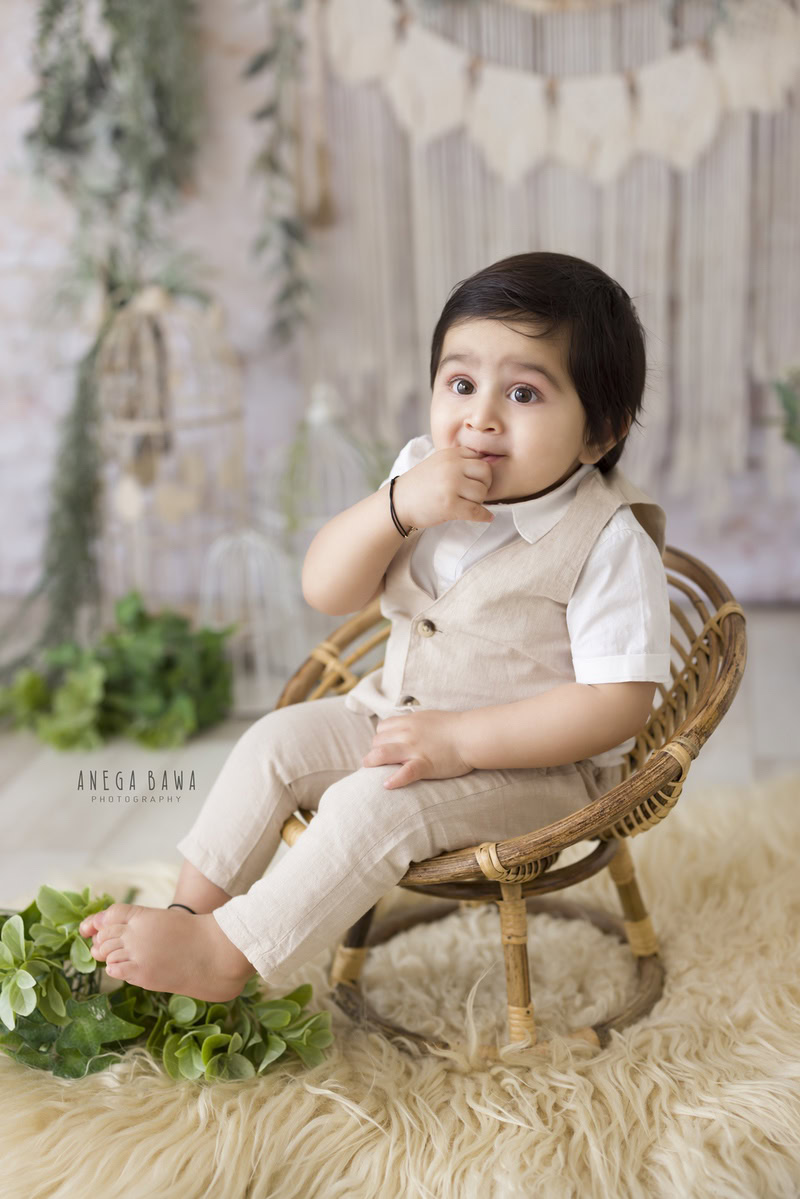 In this enchanting snapshot from a baby pre-birthday photoshoot in Delhi by Anega Bawa, a 10-month-old boy sits on a wooden chair atop a soft beige rug. The backdrop features delicate leafy fringes adorning the wall, adding a natural and charming ambiance to the scene. It's a delightful moment captured during this milestone celebration, filled with warmth and innocence.