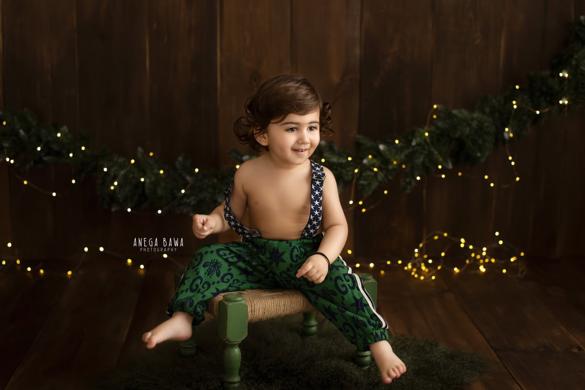 Capture precious moments of your 10-month to 1-year-old boy with a sitter photoshoot by Anega Bawa Photography in Delhi and Gurgaon. Set against a brown backdrop, let him sit on a charming woven stool, illuminated by soft golden lights, creating a warm and inviting atmosphere for timeless photographs.