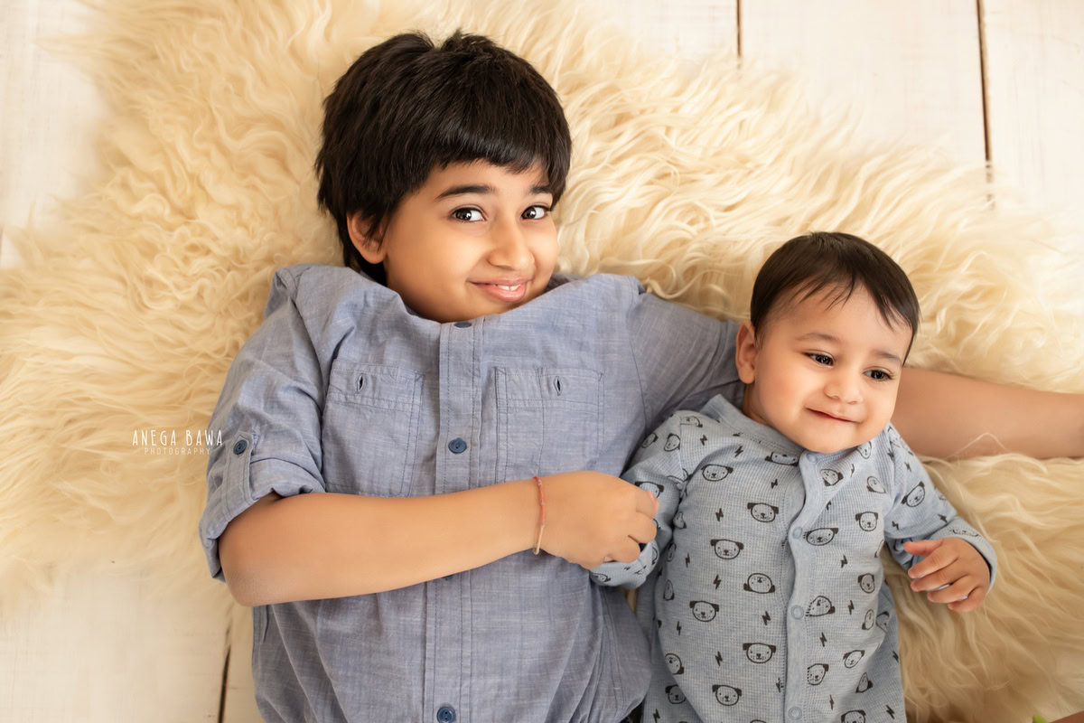 In this charming sitter photography session by Anega Bawa in Delhi, Gurgaon, a pair of siblings, aged 11 months and 1 year old, are captured together on a beige rug against a matching beige backdrop. Their bond is beautifully depicted in this heartwarming moment, creating a timeless memory for the family to cherish.