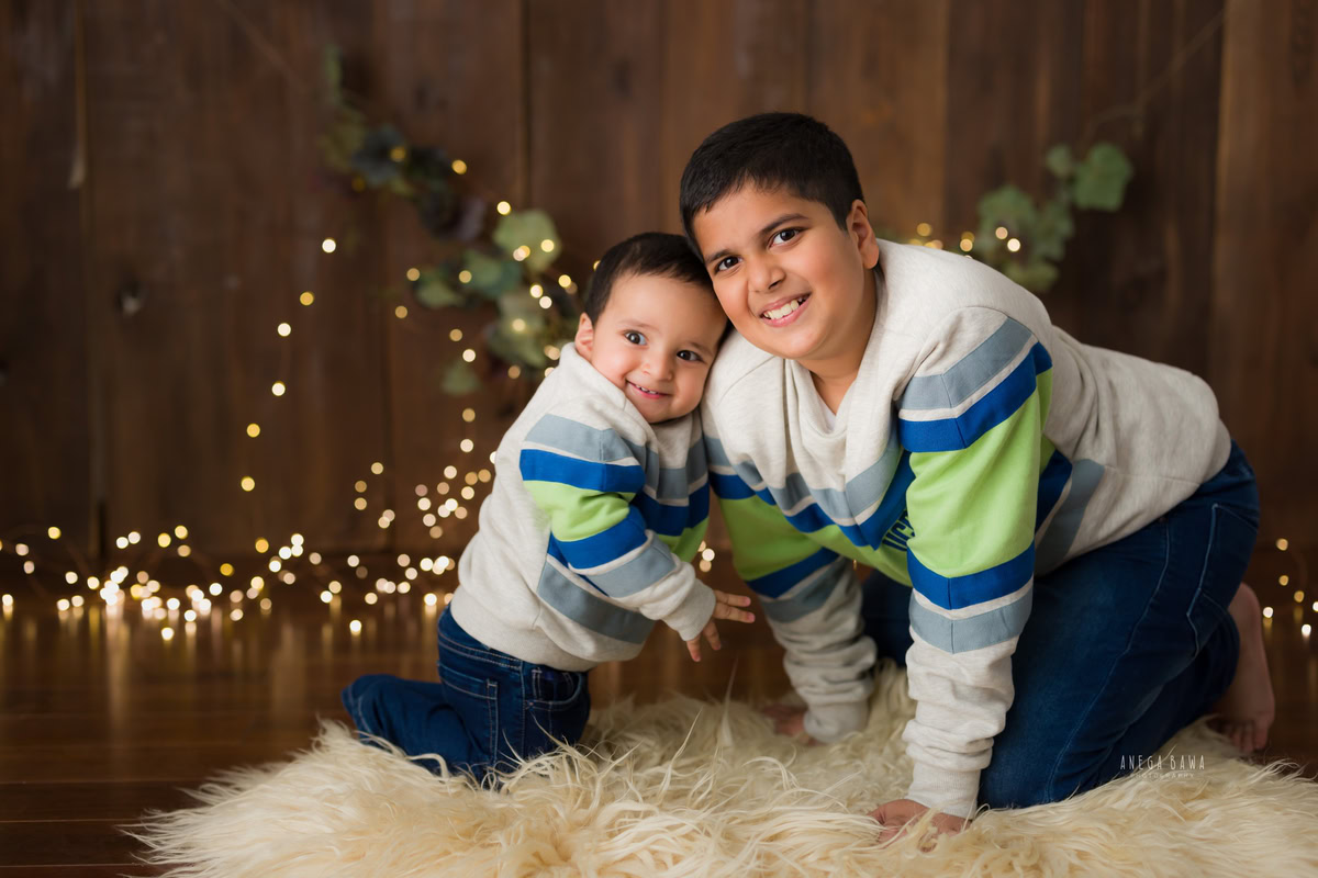 Boy with sibling on beige rug, brown backdrop, golden lights - 11 months to 1-year-old first birthday photoshoot in Delhi by Anega Bawa, Gurgaon, Noida