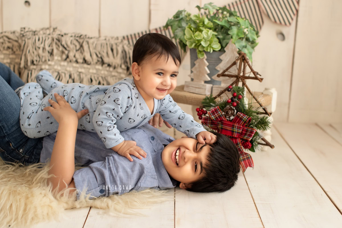 In this delightful sitter photoshoot in Delhi, Gurgaon by Anega Bawa, two siblings, aged 11 months and 1 year old, strike an adorable pose together on a beige rug against a complementary beige backdrop. The warmth of their bond shines through in this charming moment captured by the lens, creating a precious memory for their family to treasure.