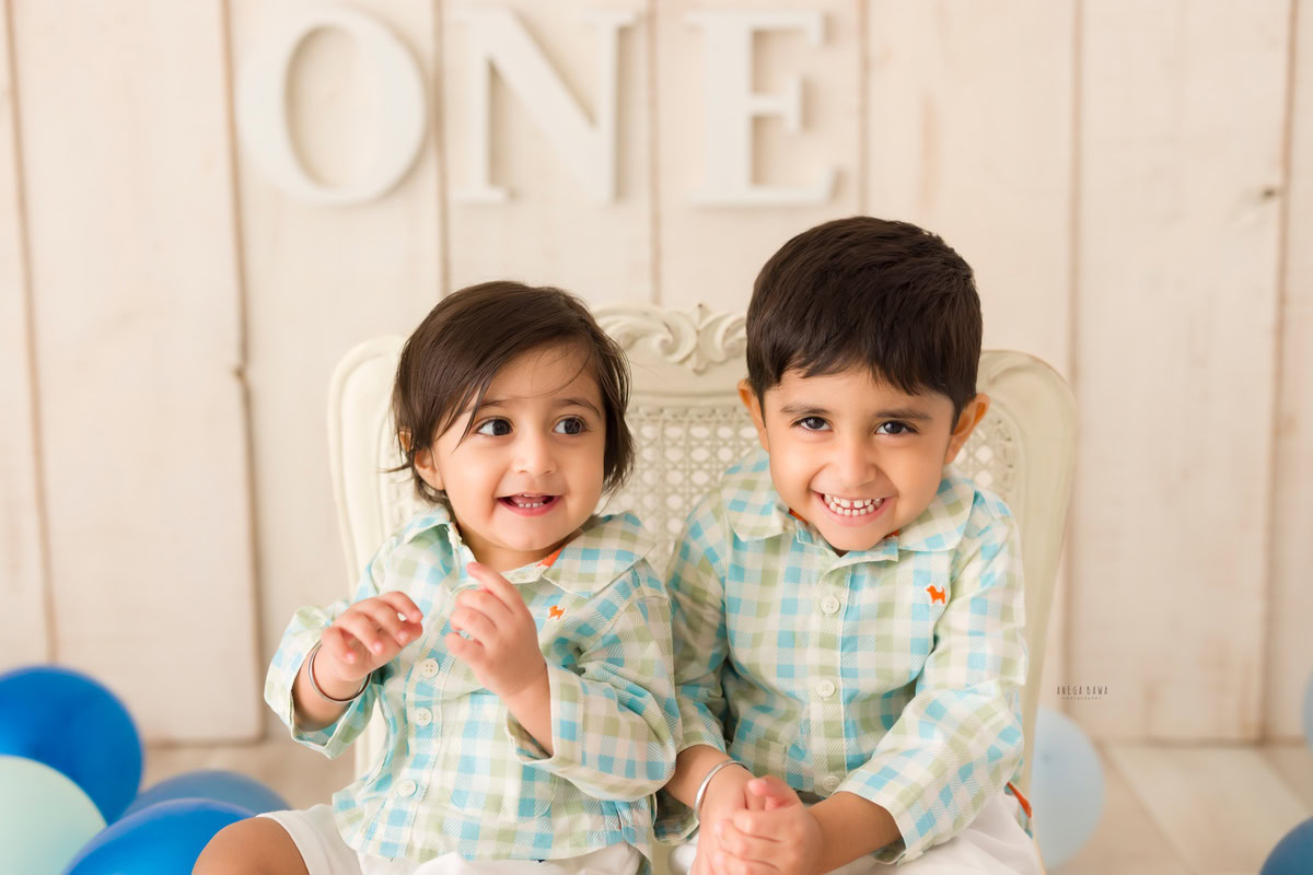 In a delightful scene captured during a baby pre-birthday photoshoot in Delhi by Anega Bawa, two adorable siblings sit together on a chair against a backdrop adorned with balloons. At 11 months and 1 year old, these little ones radiate joy and sibling camaraderie, creating a precious moment to cherish forever.