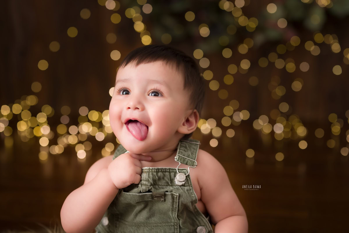 In the enchanting glow of fairy lights against a rustic brown backdrop, a cherubic 12-month-old boy is captured in a serene moment during his baby pre-birthday photoshoot. This captivating image, skillfully crafted by the renowned photographer Anega Bawa, exudes warmth and charm, embodying the essence of childhood bliss.