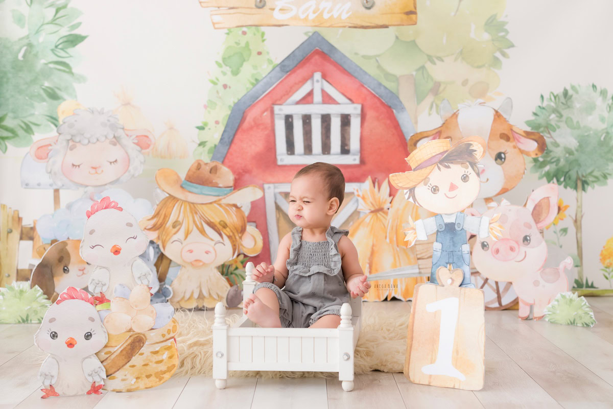 Nestled in a pristine white cot against a whimsical cartoon backdrop, the 12-month-old boy exudes pure innocence and wonder. Captured skillfully by the lens of Anega Bawa, this enchanting moment from his baby pre-birthday photoshoot in Delhi, Gurgaon, and Noida encapsulates the magic of early childhood.