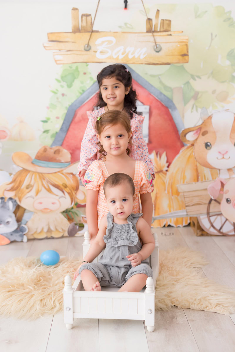 Boy seated in a pristine white cot against a whimsical cartoon backdrop, commemorating his journey from 12 months to 1 year old during his first birthday photoshoot in Delhi by Anega Bawa, Gurgaon, Noida.