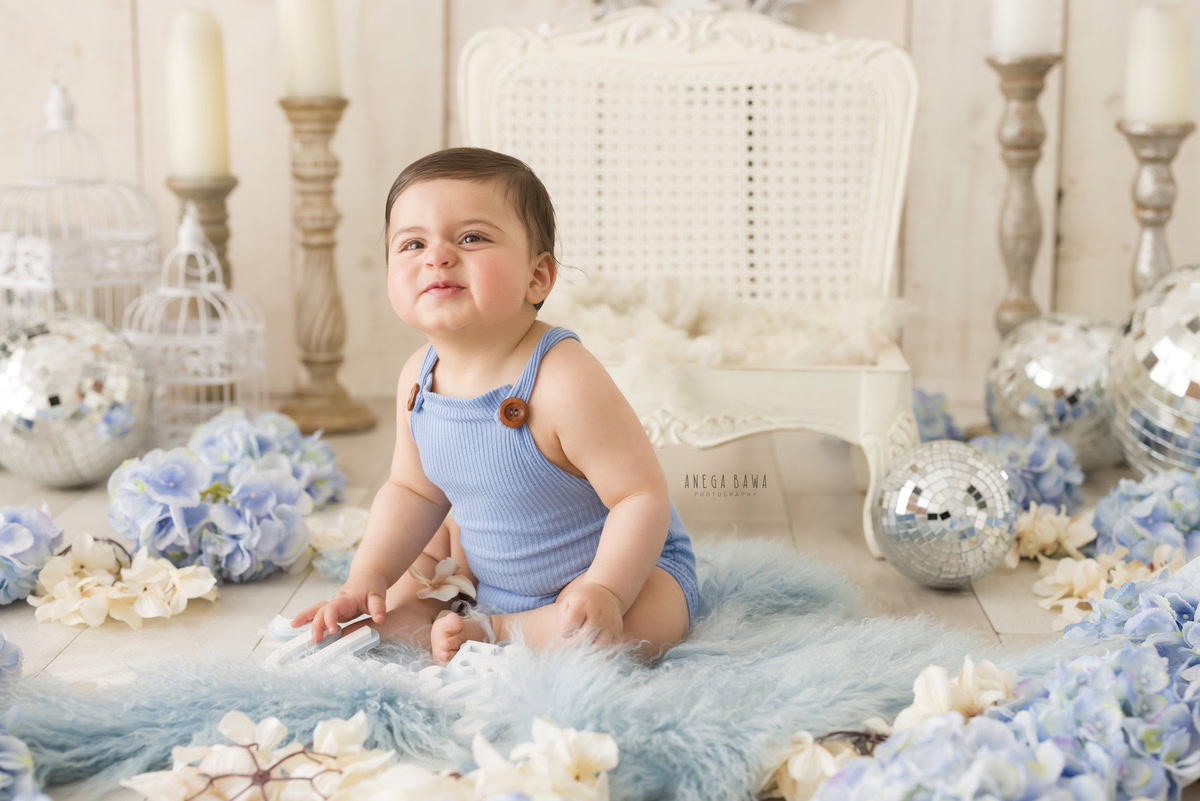 Perched upon a soft blue rug amidst delicate blue and white flowers, the 12-month-old boy is surrounded by a whimsical array of elements - from a charming candle stand to sparkling disco balls and elegant white castles. Against a soothing beige backdrop, expertly captured by Anega Bawa during his baby pre-birthday photoshoot, this enchanting scene unfolds in Delhi, Gurgaon, and Noida, offering a glimpse into the magic of his early years.