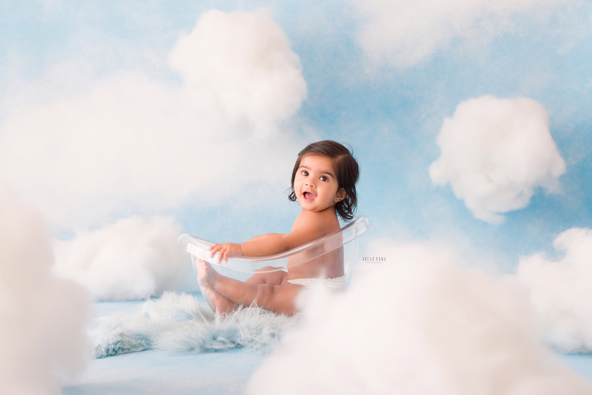 In a serene ambiance painted by a cloudy backdrop, the 12-month-old boy sits comfortably on a calming blue rug. This captivating moment, skillfully captured by Anega Bawa during his baby pre-birthday photoshoot, offers a glimpse into his early years in Delhi, Gurgaon, and Noida.