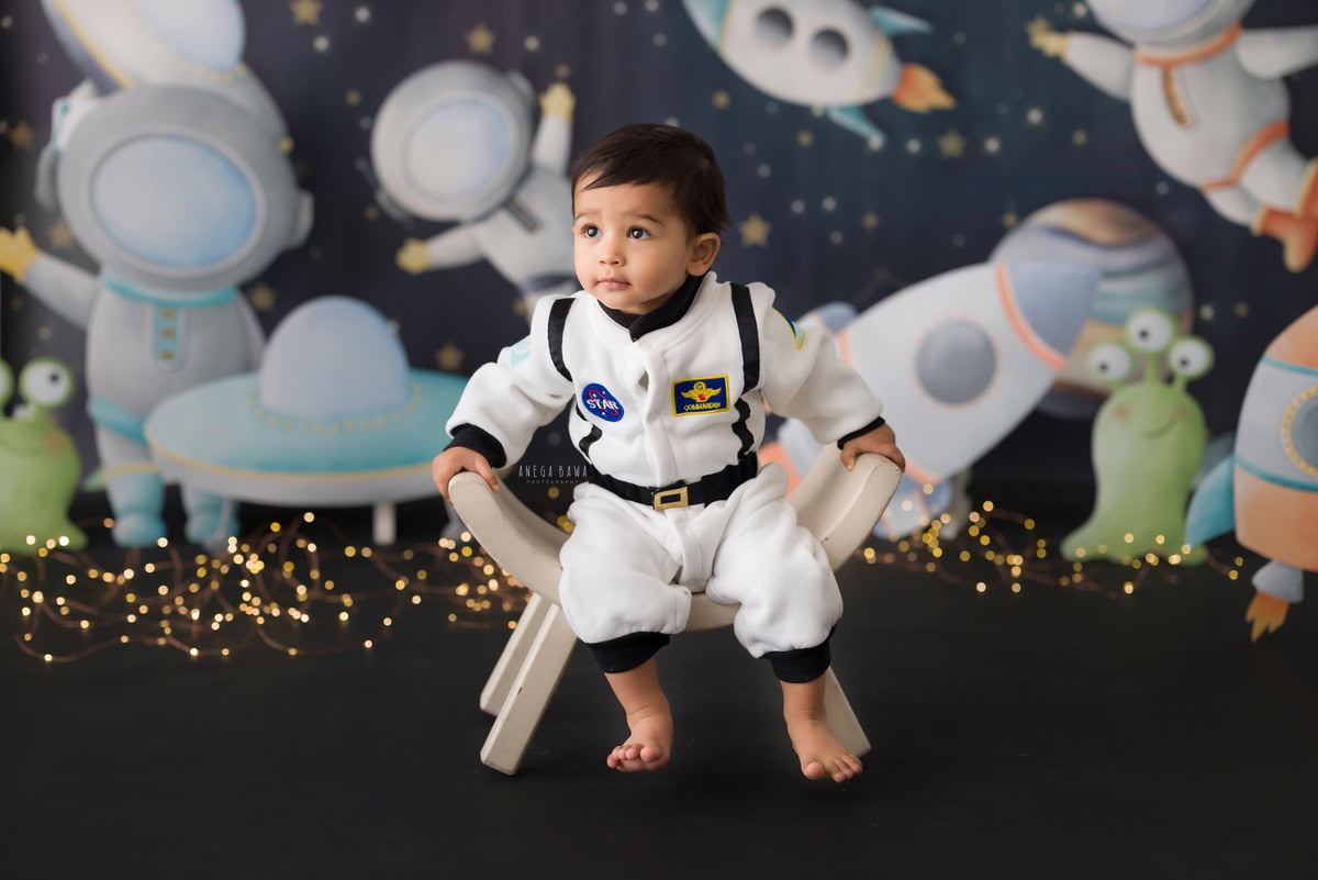 Perched on a curvy chair against a mesmerizing space-themed backdrop, the 10-month-old boy basks in the soft glow of fairy lights. This enchanting moment, captured during his baby pre-birthday photoshoot by Anega Bawa in Delhi, Gurgaon, and Noida, captures the wonder and innocence of childhood amidst the cosmic allure of the universe.