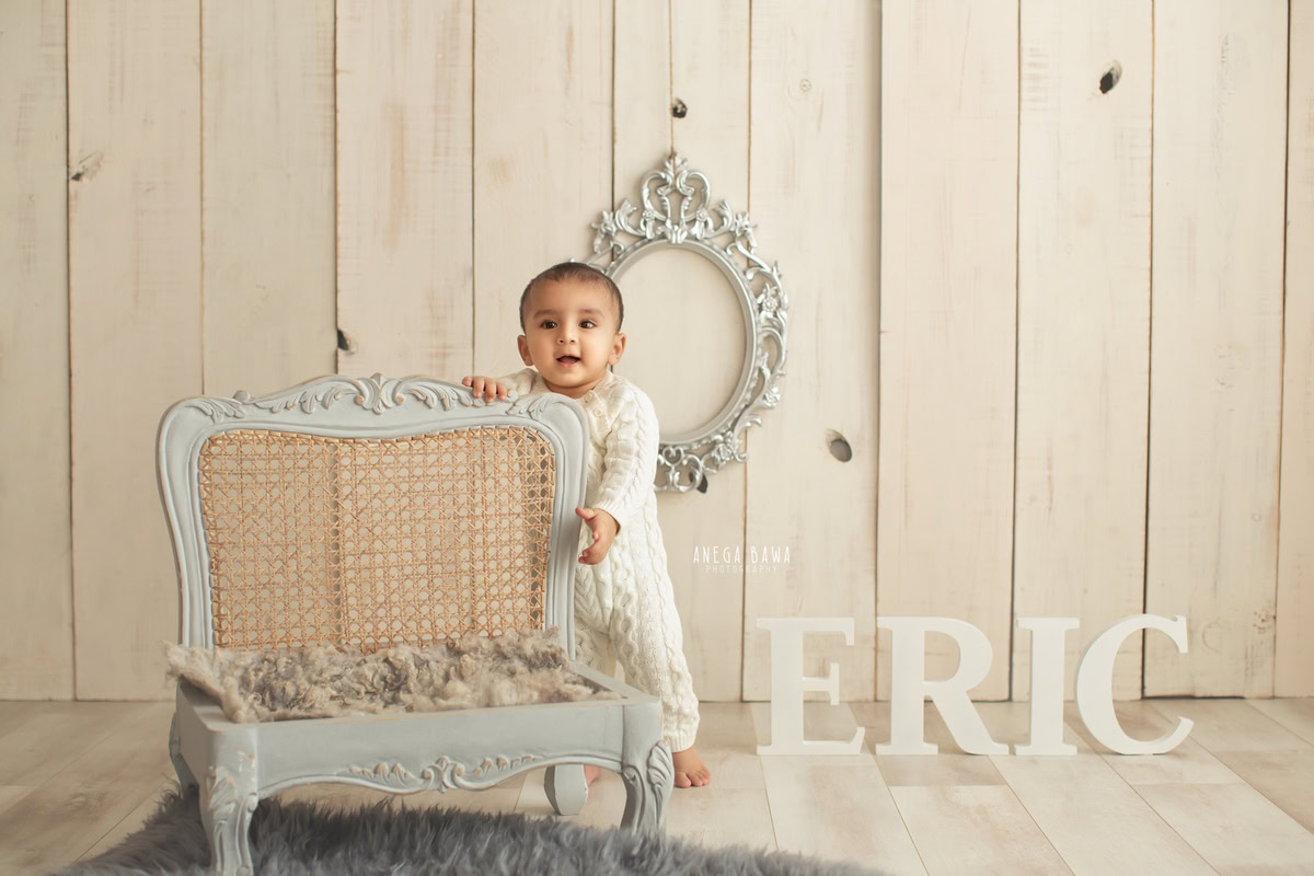 Capture the charm of your little boy's milestones with Anega Bawa Photography in Delhi and Gurgaon. Standing tall beside a grey chair against a soothing beige backdrop, adorned with a silver frame and a personalized name frame on the wall, your 8-month to 1-year-old shines in every frame, creating treasured memories to last a lifetime.