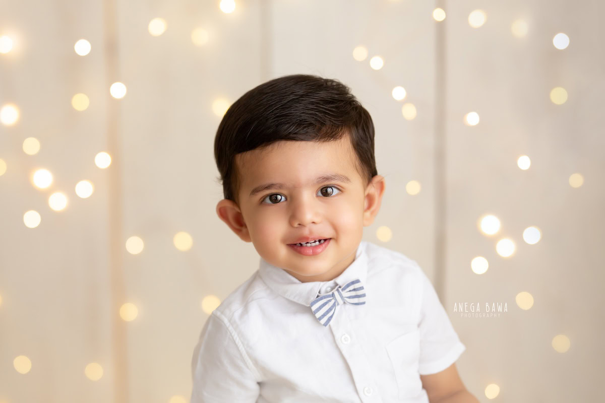 Watch your little prince glow with joy in a photoshoot by Anega Bawa Photography in Delhi and Gurgaon. Dressed in a charming bow and surrounded by twinkling fairy lights against a soothing beige backdrop, your 12-month to 1-year-old creates enchanting memories to cherish forever.