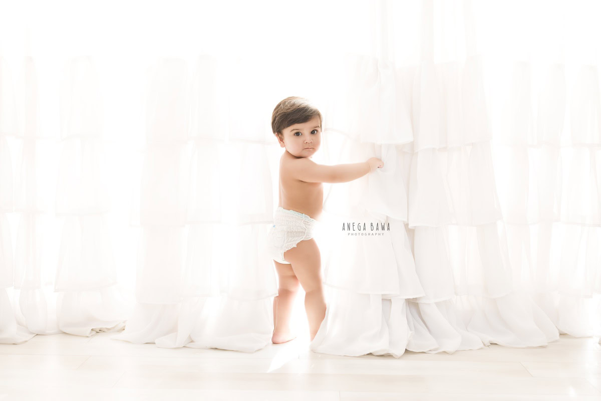 In this delightful sitter photography session in Delhi, Gurgaon by Anega Bawa, a charming 12-month-old boy stands gracefully against a pristine white backdrop. Dressed in cozy Pampers, he exudes innocence and joy, radiating pure happiness. This timeless moment captures the essence of childhood, creating cherished memories that will last a lifetime.
